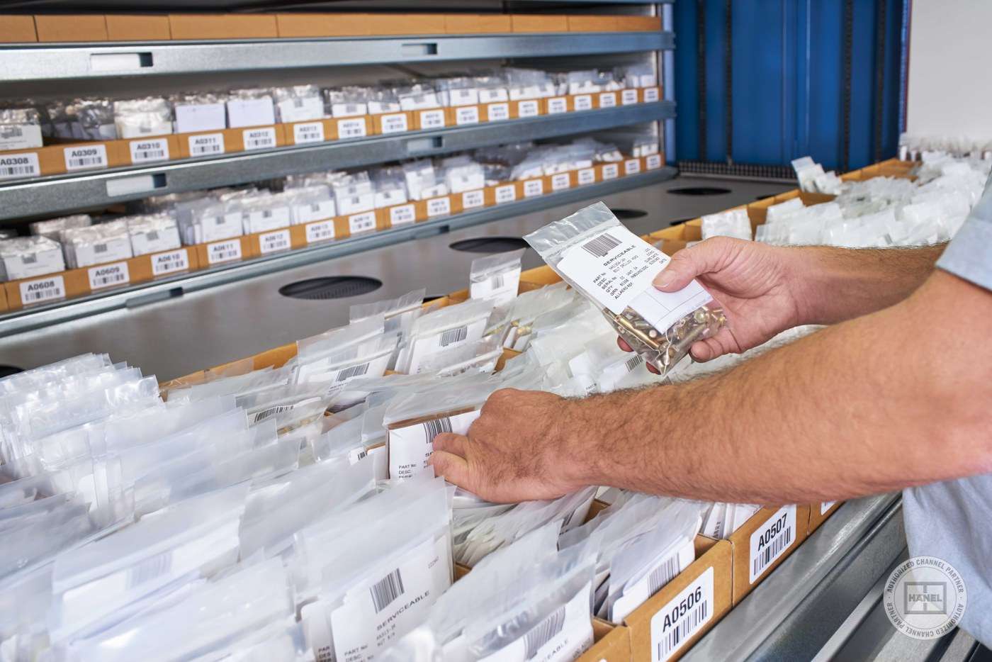 An operator picking a labeled bag of parts from a Hänel storage tray